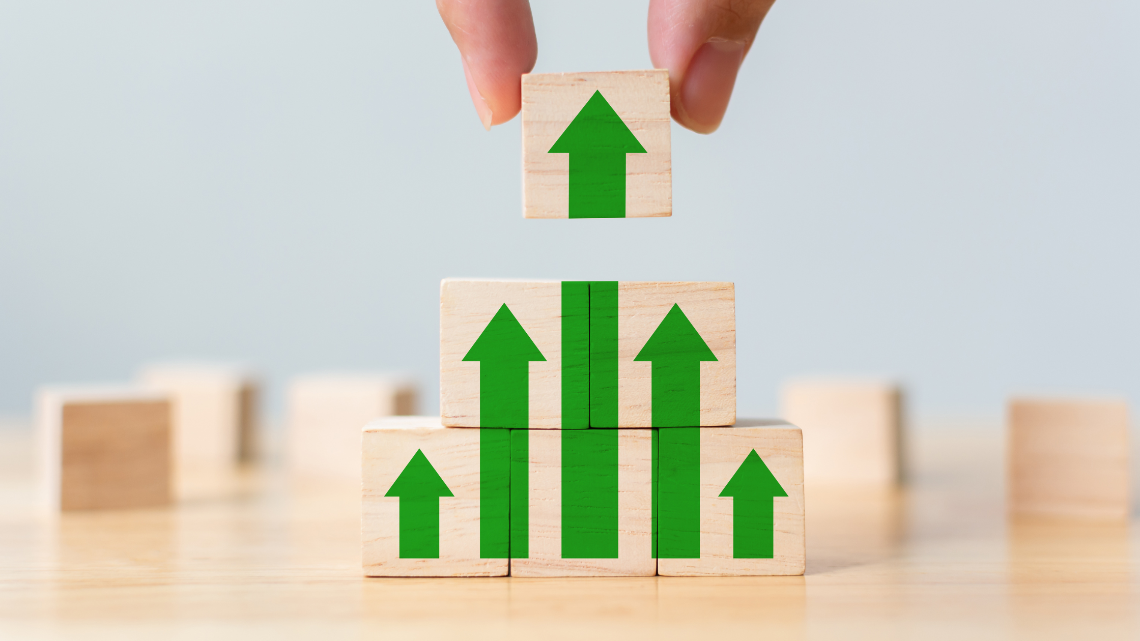 A hand placing a wooden block on top of other wooden blocks depicting green arrows pointing upwards