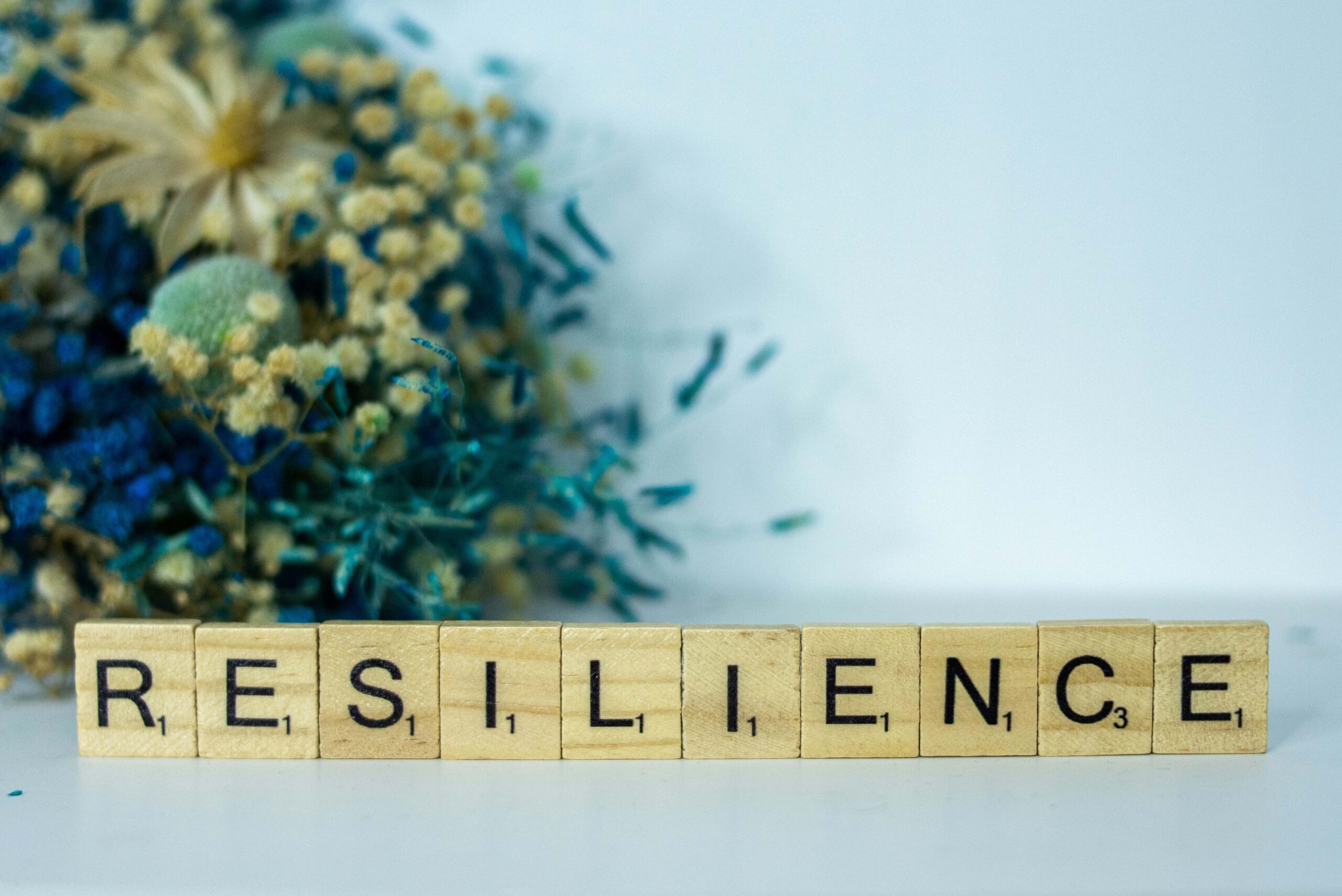 Wooden blocks with black letters on them that spell out 'resilience'. There are flowers in the background