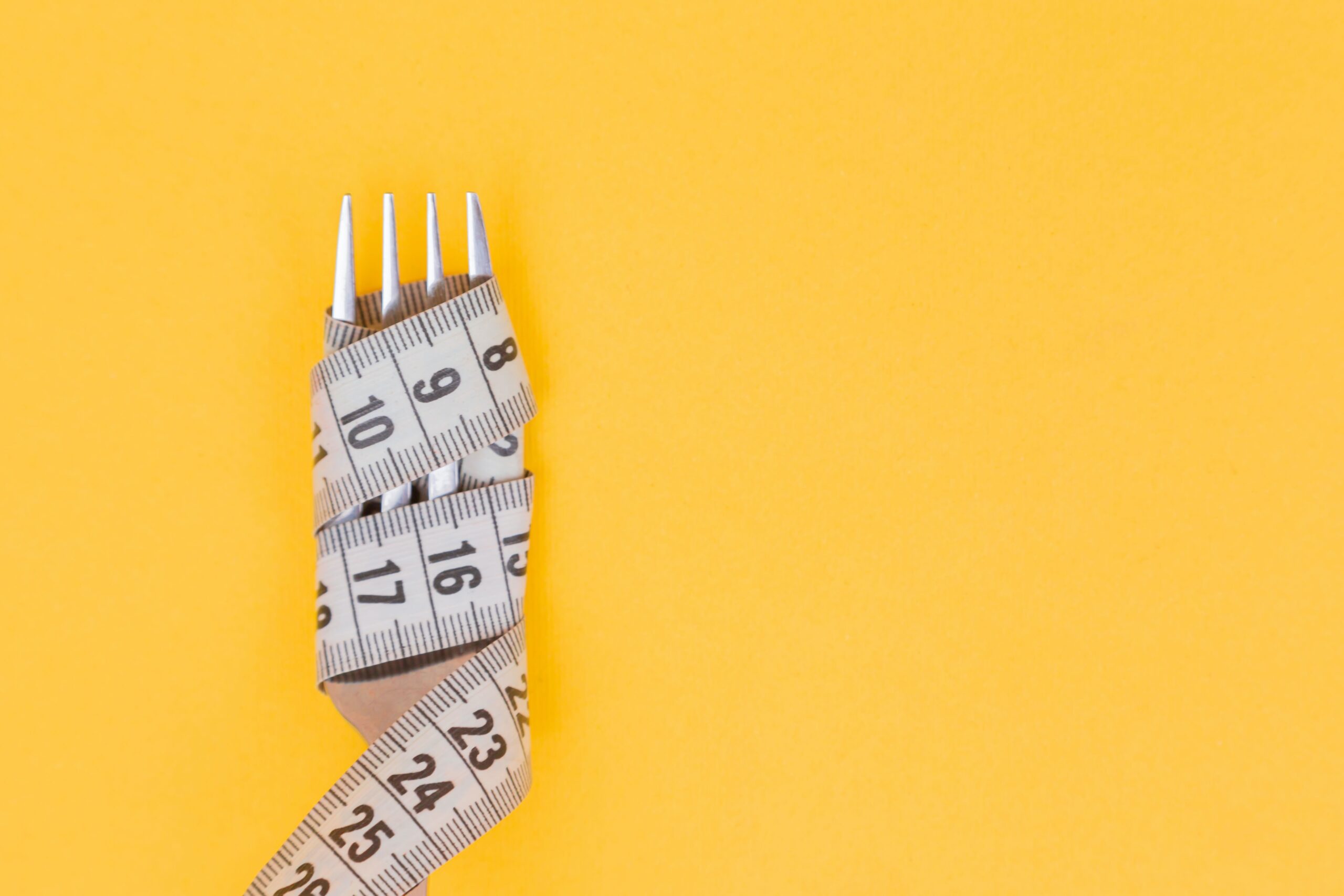 A fork wrapped in a tape measure on a yellow background