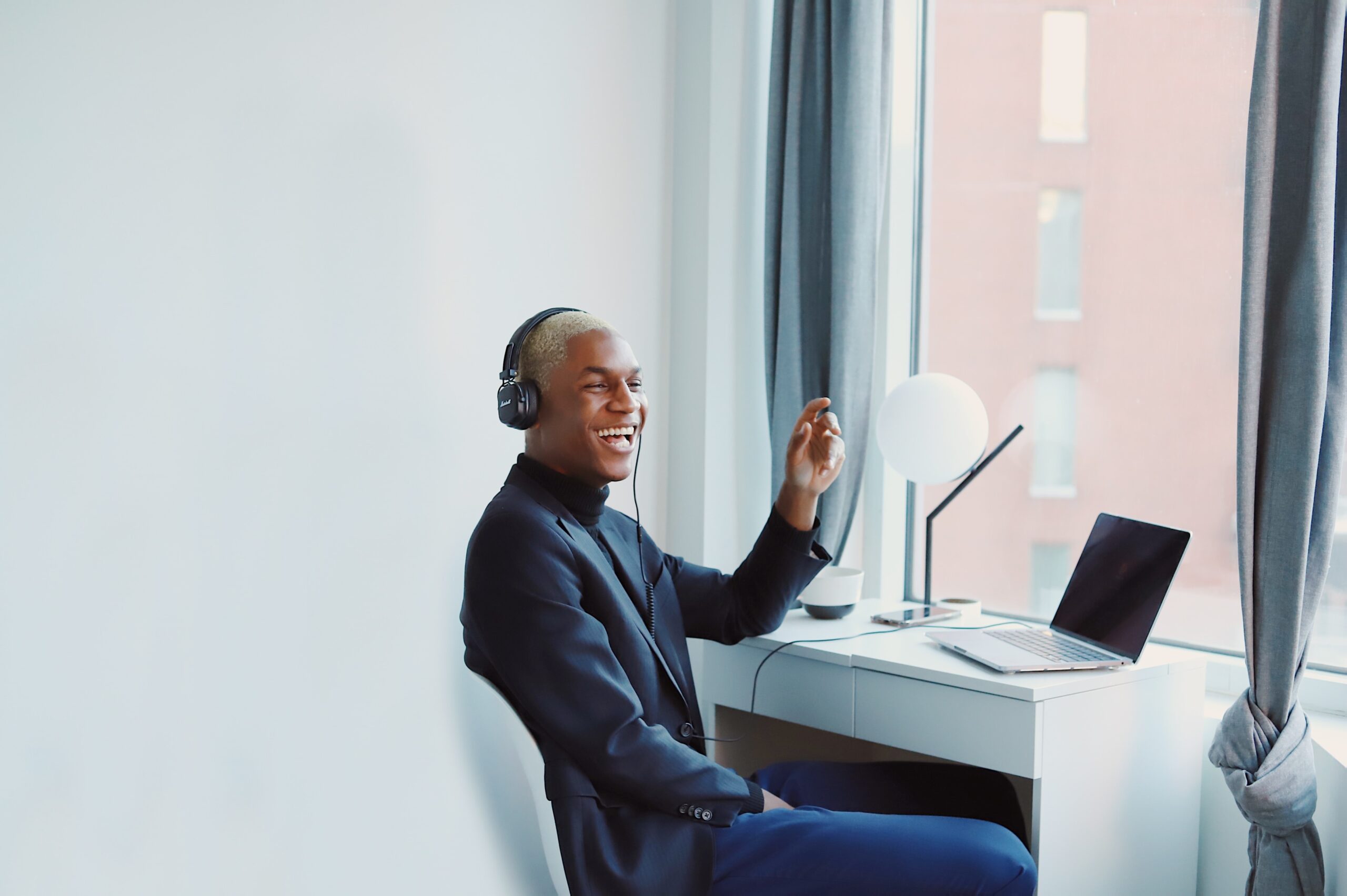 A man wearing dark clothes sitting at a white desk facing an open window