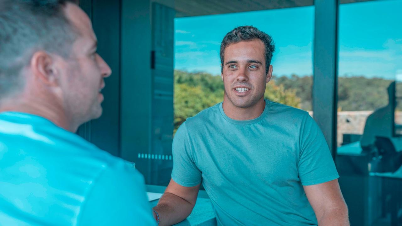 Two men wearing blue t-shirts having a conversation in front of glass windows